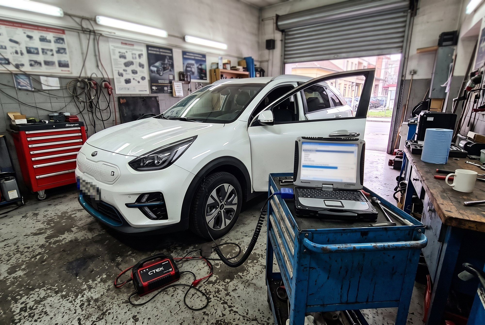 Diagnostic laptop connected to an electric Kia in a workshop during a software update